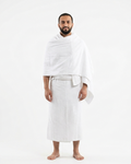 A man standing against a plain white studio background, wearing a white robe with a shawl draped over his shoulders.