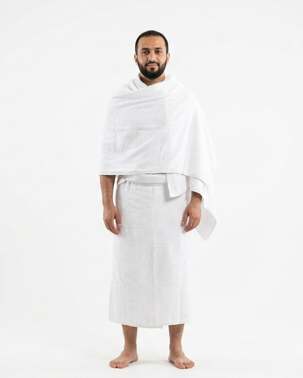 A man standing against a plain white studio background, wearing a white robe with a shawl draped over his shoulders.